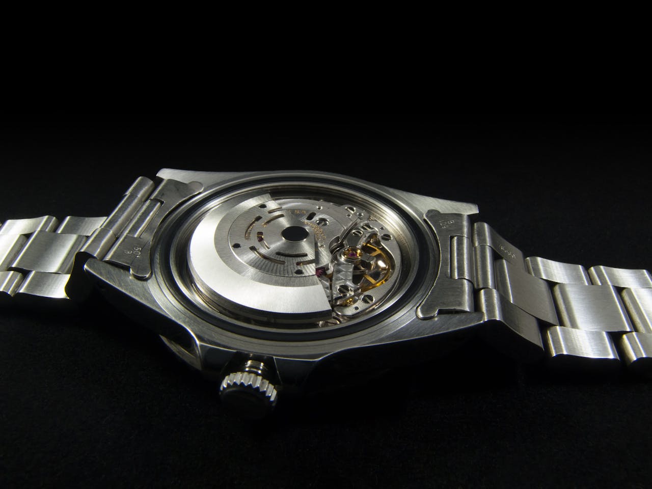 Intricate view of a silver analog watch showcasing detailed gear and mechanism against a black background.