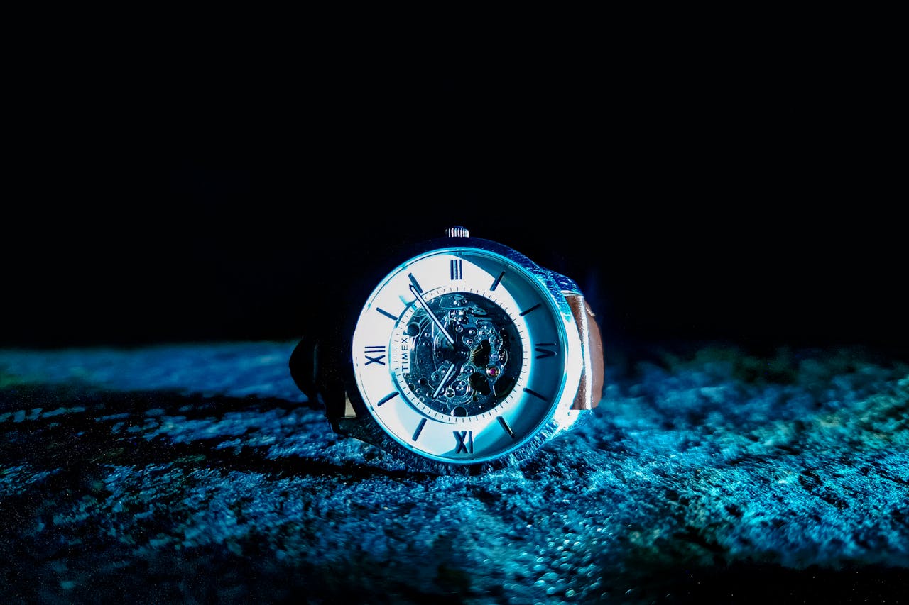 Close-up of a mechanical watch with Roman numerals, illuminated in dramatic lighting.